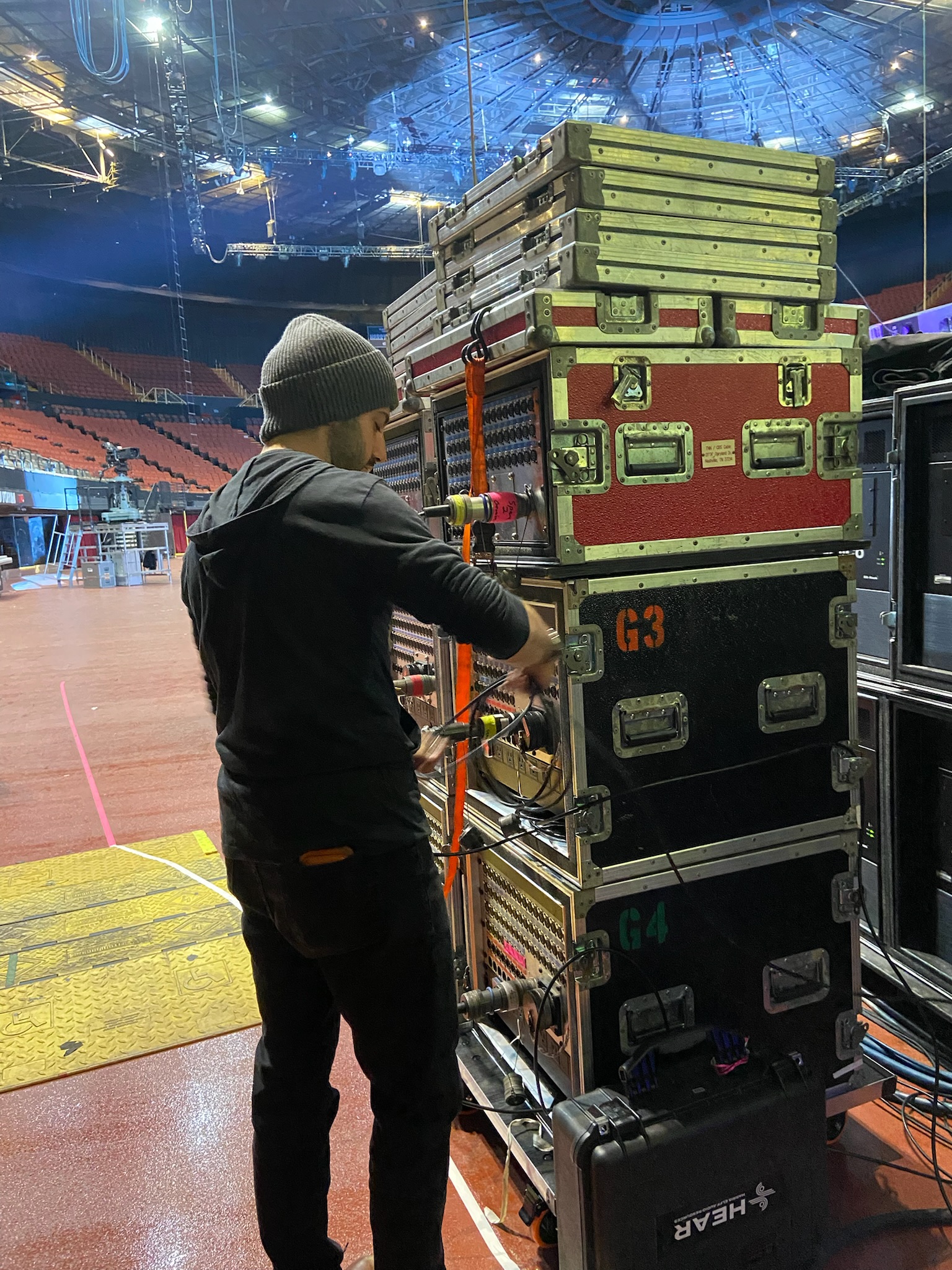 FireAid 2025 — RPG crew member working stacked road cases on the Kia Forum floor at load-in